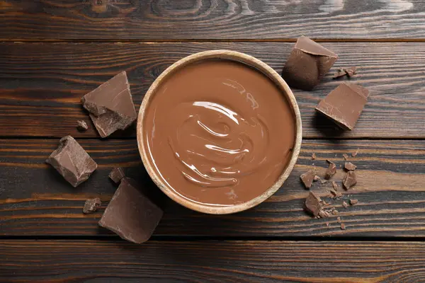 Tasty milk chocolate paste in bowl and pieces on wooden table, top view