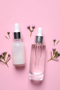 Kozmetik serumlar ve pembe arka planda güzel çiçekler.