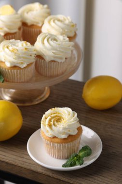 Beyaz kremalı lezzetli limonlu kekler, ahşap masada nane ve limon, yakın plan.