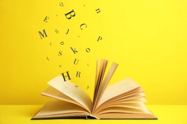 Sarı arka planda üzerinde harfler uçuşan açık bir kitap.