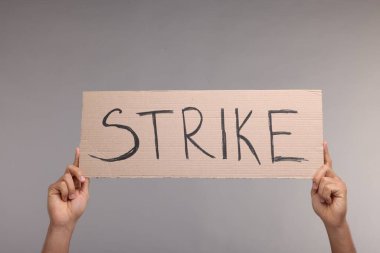 Gri arka planda kelime grevi yazılı karton pankart tutan adam, yakın plan