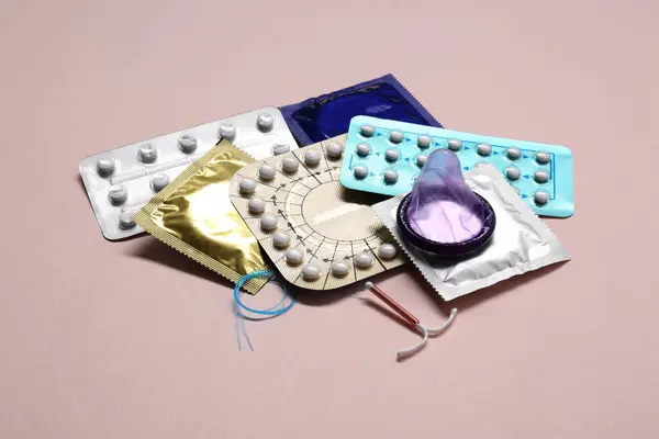 Contraceptive pills, condoms and intrauterine device on beige background. Different birth control methods