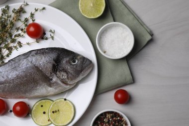 Düz kompozisyon, çiğ dorado balığı ve baharatlarla bembeyaz ahşap masada.