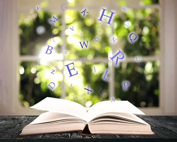 Open book with letters flying out of it on wooden table against blurred background