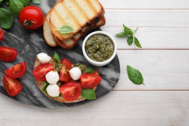 Beyaz ahşap masada mozarella, domates, fesleğen ve pesto soslu lezzetli Caprese sandviçi.