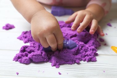 Küçük çocuk beyaz tahta masada kinetik kumla oynuyor, yakın plan.