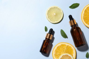 Kozmetik serumu şişeleri, dilimlenmiş narenciye meyveleri ve açık mavi arka planda yeşil yapraklar. Metin için boşluk