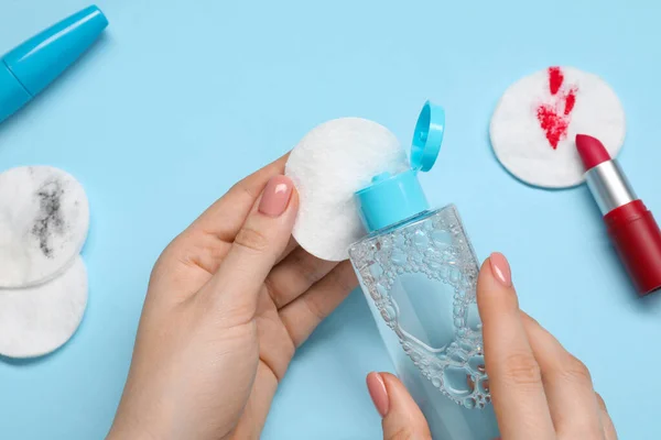 Woman using makeup remover, closeup. Cotton pads, lipstick and mascara on light blue background, top view