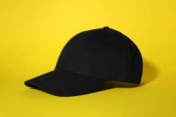 Stylish black baseball cap on yellow background