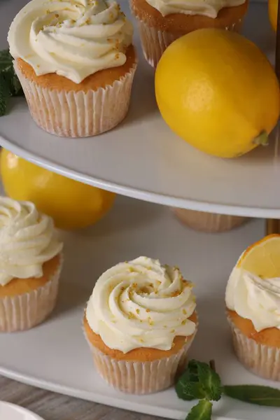 Delicious lemon cupcakes with white cream and lemons on table, closeup