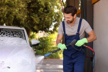 Worker washing auto with high pressure water jet at outdoor car wash