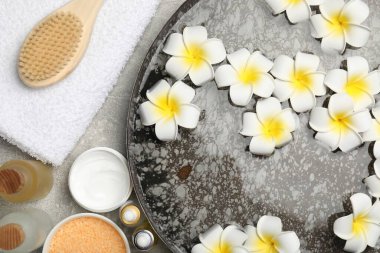 Çiçekli bir kase su ve açık gri masada farklı spa malzemeleri.