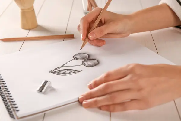 白い木のテーブルでスケッチブックのグラファイトの鉛筆でチェリーを描く女性 クローズアップ — ストック写真