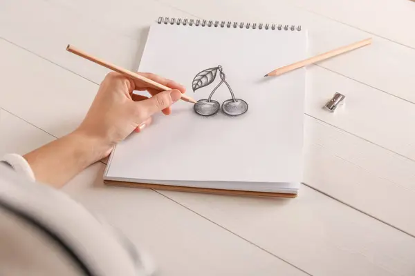白い木のテーブルでスケッチブックのグラファイトの鉛筆でチェリーを描く女性 クローズアップ — ストック写真
