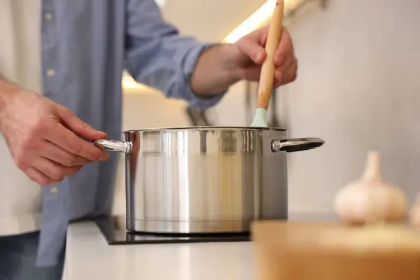 Man cooking delicious soup in kitchen, closeup
