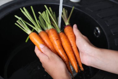 Olgun havuçları lavaboda akan suyla yıkayan kadın, yakın plan.