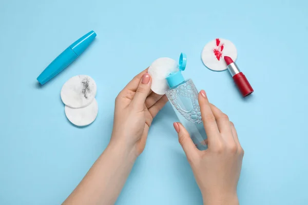 Woman using makeup remover, closeup. Cotton pads, lipstick and mascara on light blue background, top view