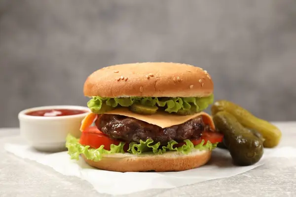 Tasty hamburger with patty, sauce and pickles on light grey table, closeup