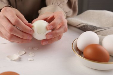 Beyaz ahşap masada haşlanmış yumurta soyan kadın, yakın plan.