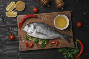 Düz kompozisyon, taze çiğ dorado balığı ve siyah ahşap masa üzerindeki baharatlar.