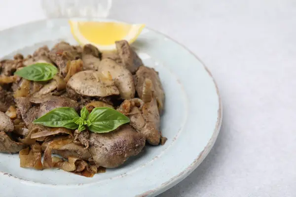 Delicious fried chicken liver with onion and basil on light table, closeup. Space for text