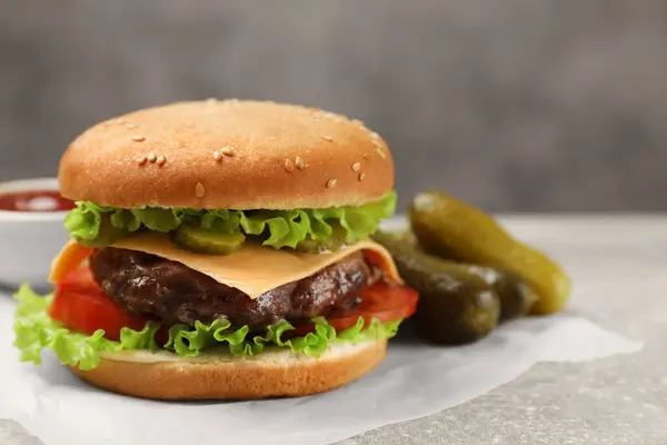 Tasty hamburger with patty and pickles on light grey table, closeup. Space for text