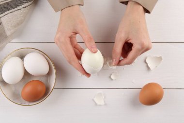 Beyaz ahşap masada haşlanmış yumurta soyan kadın.