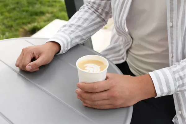 Coffee to go. Man with paper cup of drink at grey table outdoors, closeup
