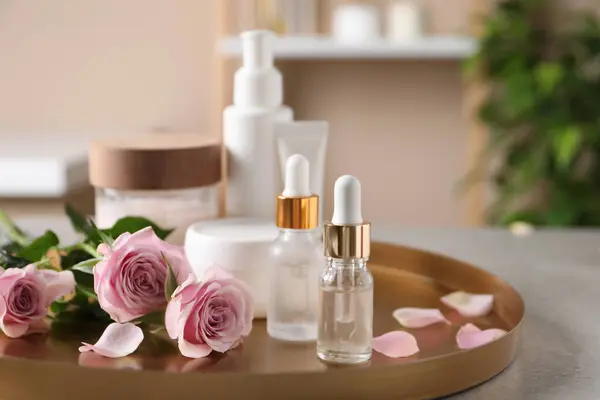 Bottles of cosmetic serum, beauty products and flowers on table indoors