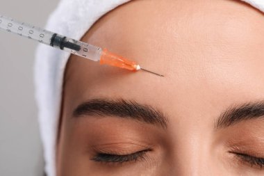Genç bir kadın açık gri arka planda yüz enjeksiyonu yaptırıyor, yakın plan. Estetik ameliyat