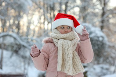 Kış günü kar parkında Noel Baba şapkası takan tatlı küçük kız.