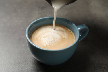Gri masadaki kahve fincanına süt dökülüyor, yakın plan.