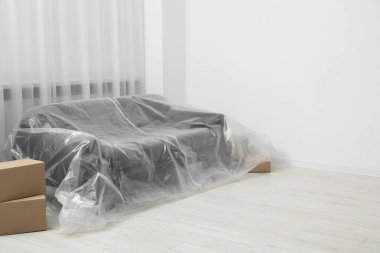 Stylish sofa covered with plastic film and boxes at home. Space for text clipart