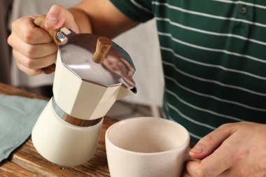 Moka pot 'tan ahşap masa içerisindeki fincana aromatik kahve döken bir adam.