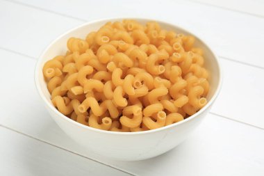 Beyaz ahşap masada kasede çiğ cavatappi makarna, yakın plan.