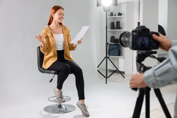 Casting call. Woman with script performing while camera operator filming her against light grey background in studio