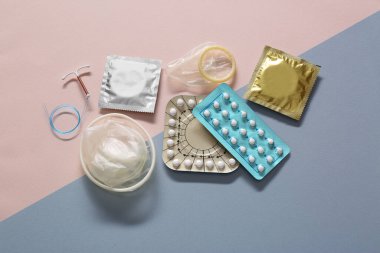 Doğum kontrol hapları, prezervatifler ve bej arka planda rahim içi cihazlar. Farklı doğum kontrol yöntemleri
