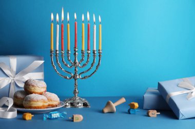 Hanuka kutlaması. Açık mavi masada yanan mumlar, dreideller, çörekler ve hediye kutuları olan Menorah, metin için yer
