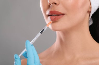 Doktor açık gri arka planda genç bir kadına dudak iğnesi yapıyor, yakın plan. Estetik ameliyat