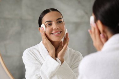 Güzel kadın içeride aynanın yanında pamuk pedlerle makyaj yapıyor.