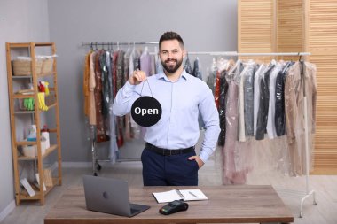 Kuru temizleme servisi. Mutlu işçi işyerinde açık tabela tutuyor.