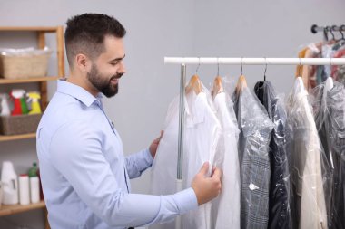 Kuru temizleme servisi. Mutlu işçi, içerideki askılardan kıyafet seçiyor.