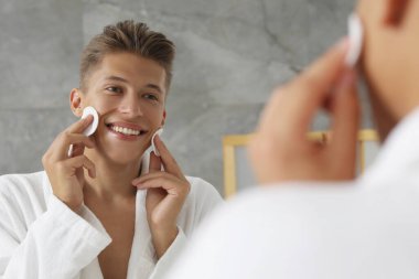 Banyoda aynanın yanında pamuklu pedleri olan yakışıklı bir genç.