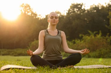 Güneşli bir günde dışarıda yoga yapan güzel bir kadın. Lotus pozu