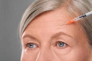 Son sınıf öğrencisi kadın açık gri arka planda yüz enjeksiyonu yaptırıyor, yakın plan. Estetik ameliyat