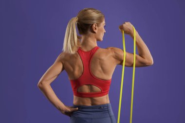 Atletik kadın mor arka planda elastik direniş bandıyla egzersiz yapıyor.
