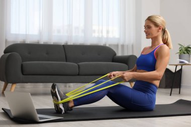 Spor yapan atletik bir kadın evde spor yaparken lastikli bant takıyor.