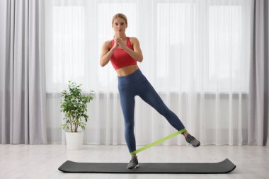 Spor yapan atletik bir kadın evde spor yaparken lastikli bant takıyor.