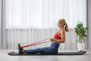 Spor yapan atletik bir kadın evde spor yaparken lastikli bant takıyor.