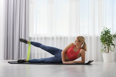 Spor yapan atletik bir kadın evde spor yaparken lastikli bant takıyor.